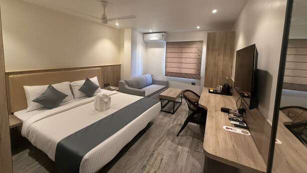 Quarto de hotel moderno com uma cama grande, um sofá, uma escrivaninha e uma televisão.