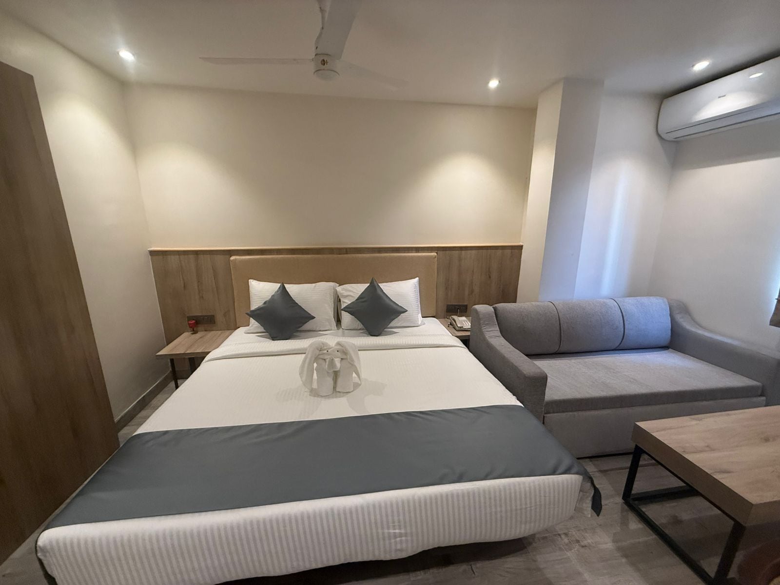A hotel room with a large bed, a sofa, a small table, and a ceiling fan.