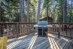 Una terraza con una parrilla y una cabaña pequeña en un bosque.