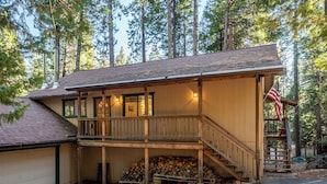 A wooden cabin with a covered porch, a garage, and a stack of firewood. - Bennetts’ Bear Den | Game Room • Cozy Forest Cabin (Dorrington)