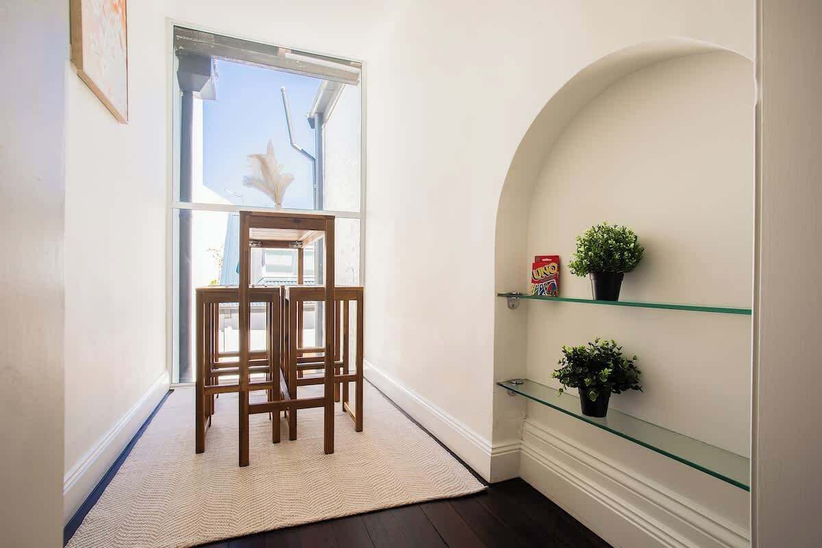 A hallway with a wooden chair, a glass shelf with plants, and a door leading to a room.