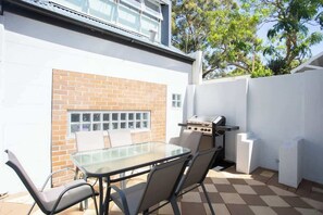 Eine Terrasse mit Glastisch und -stühlen, einem Grill und einer Ziegelwand.
