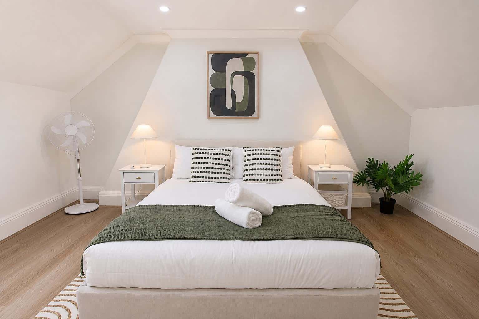 Ein Schlafzimmer mit einem großen Bett, zwei Nachttischen, einer Stehlampe, einem Wandbild und einer Zimmerpflanze.