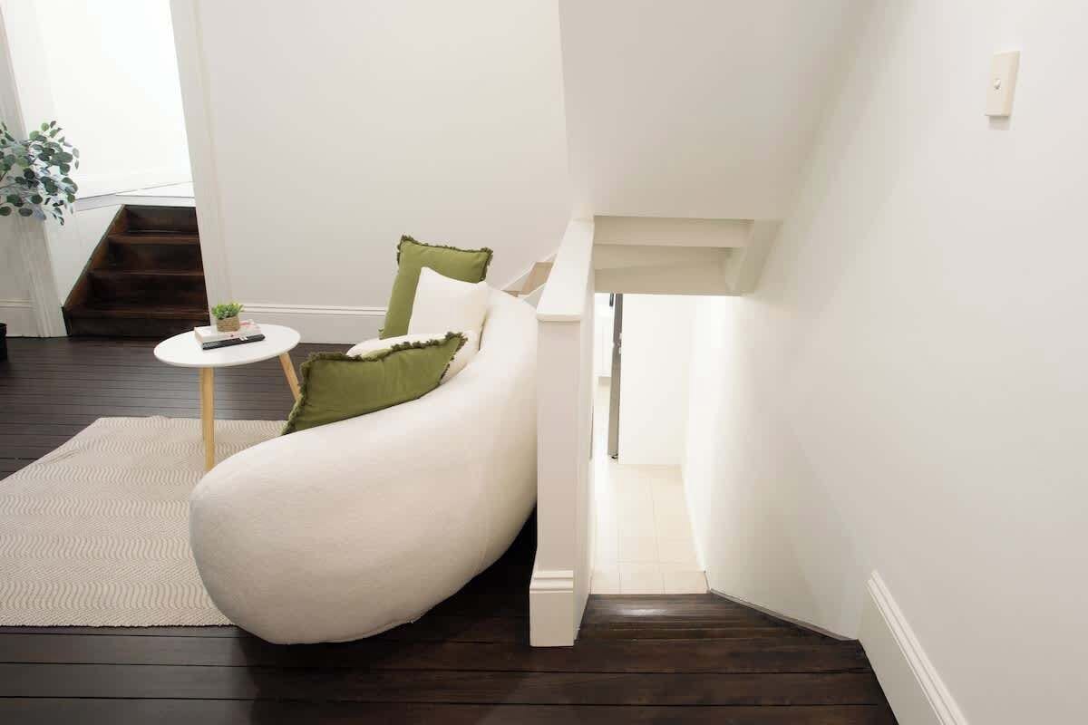 A modern living room with a curved white sofa, a small round table, and a green pillow.