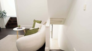 Ein modernes Wohnzimmer mit einer gebogenen weißen Couch, einem kleinen runden Tisch und einem grünen Kissen.