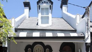 Ein zweistöckiges Gebäude mit einer symmetrischen Fassade, einem zentralen Eingang mit einer schwarzen Tür und einem kleinen Balkon darüber.