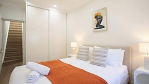 Ein Hotelzimmer mit Bett, einem Gemälde, einem Nachttisch und einer Tür.