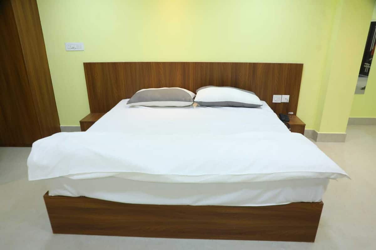 Un lit bien fait, avec une tête de lit en bois, une table de chevet avec une lampe et une prise électrique au mur.