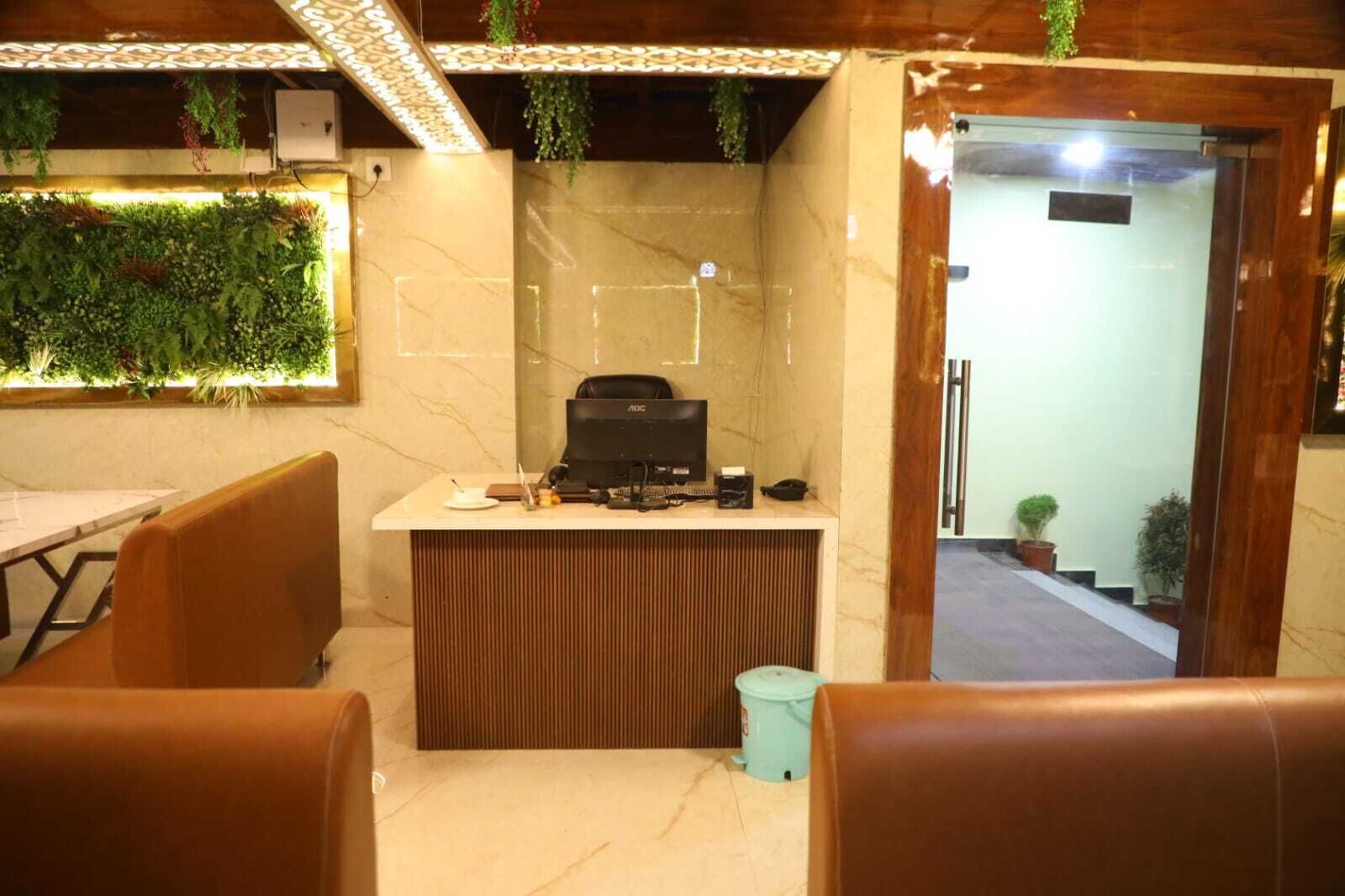 A reception desk with a computer, a trash bin, and a potted plant. There are brown leather chairs and a table in the foreground.