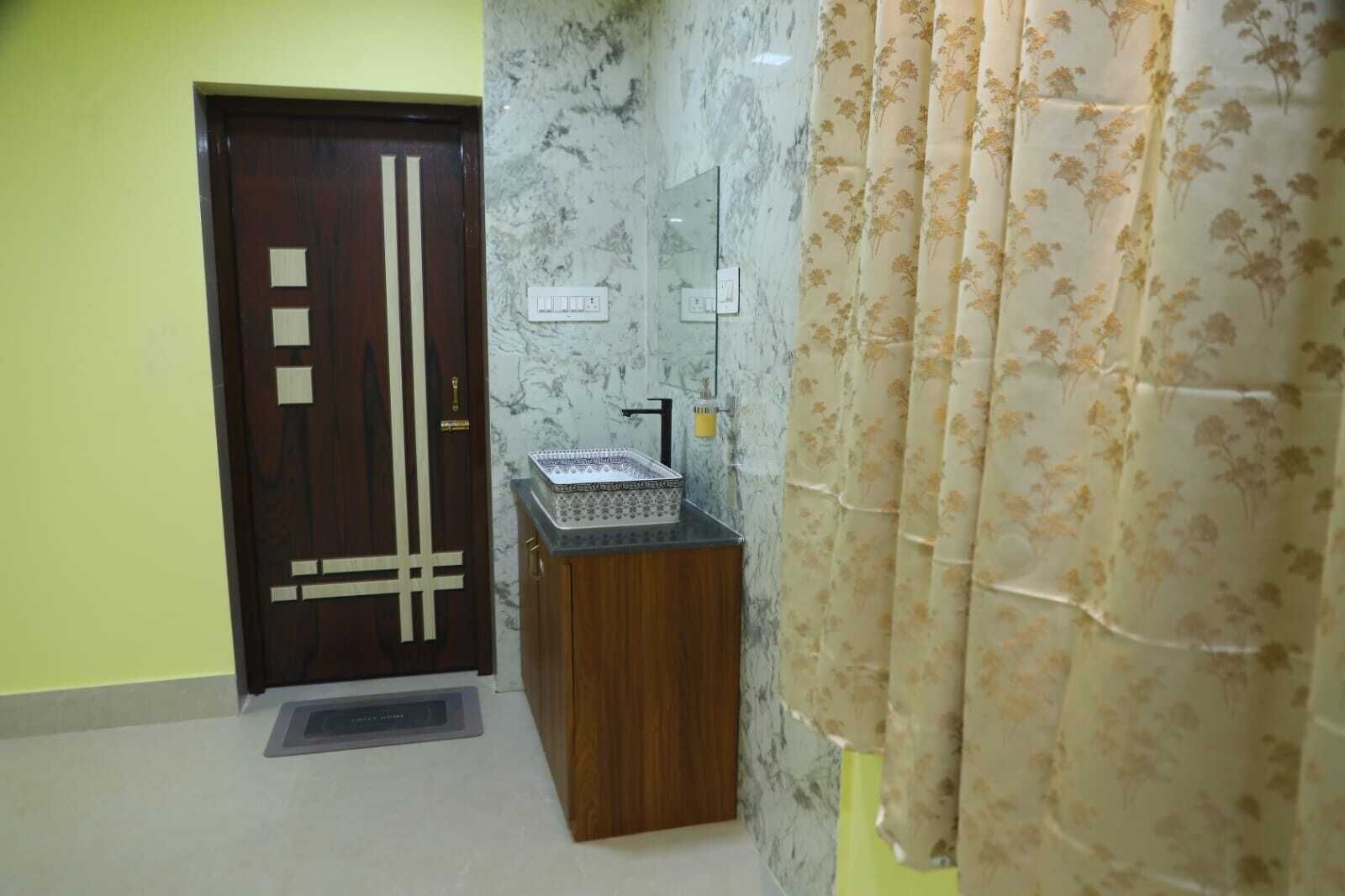 A bathroom with a wooden door, a marble wall, a sink with a mirror, and floral curtains.