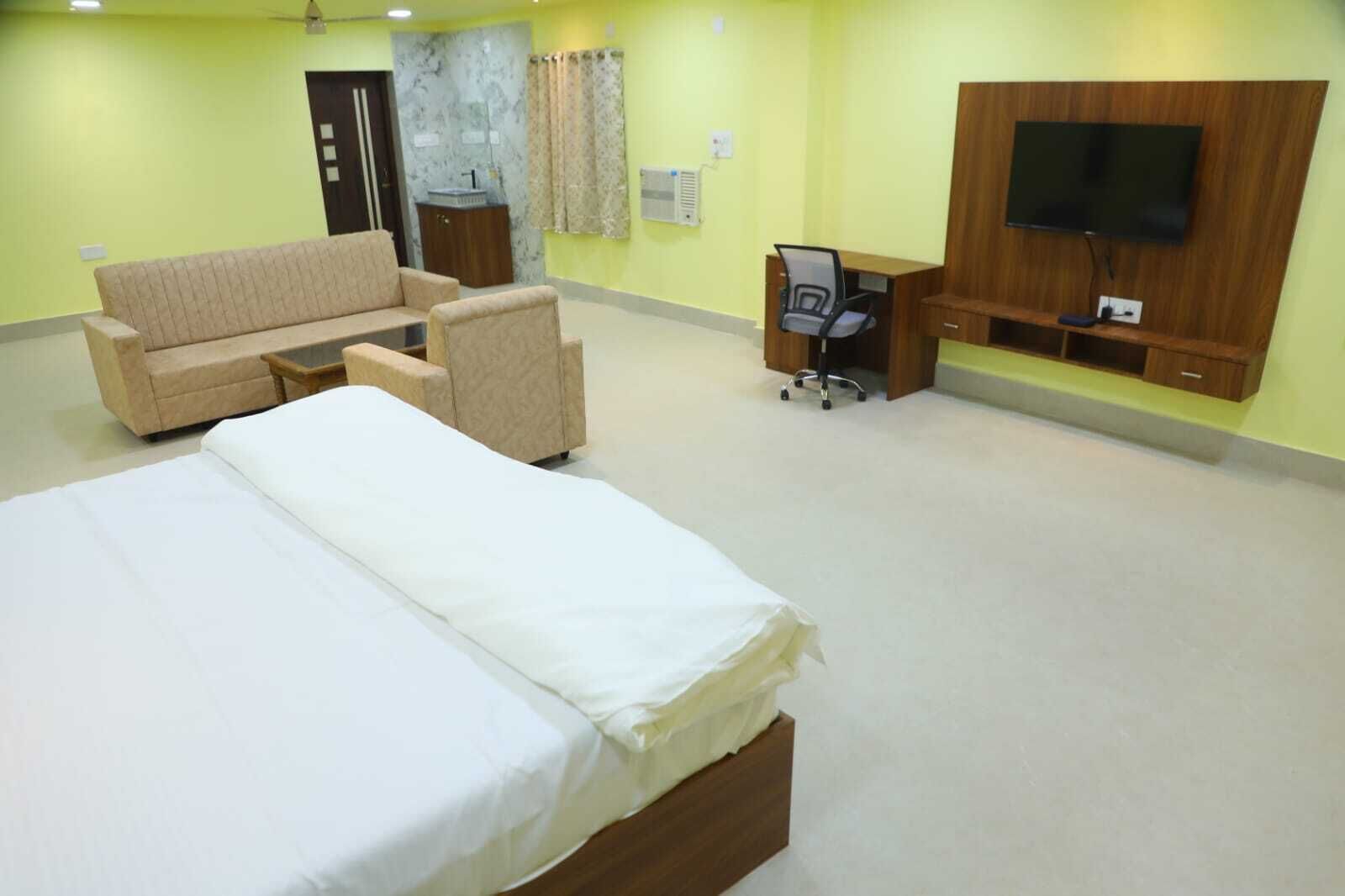 A hotel room with a bed, a sofa, a chair, a desk, and a TV.