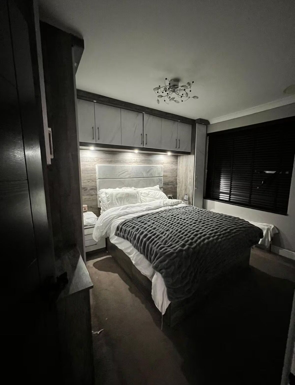 A bedroom with a bed, a nightstand, a wardrobe, and a window with blinds.