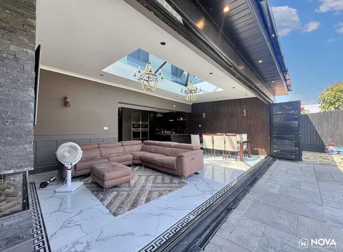 A modern living room with a sectional sofa, a fan, and a glass ceiling.