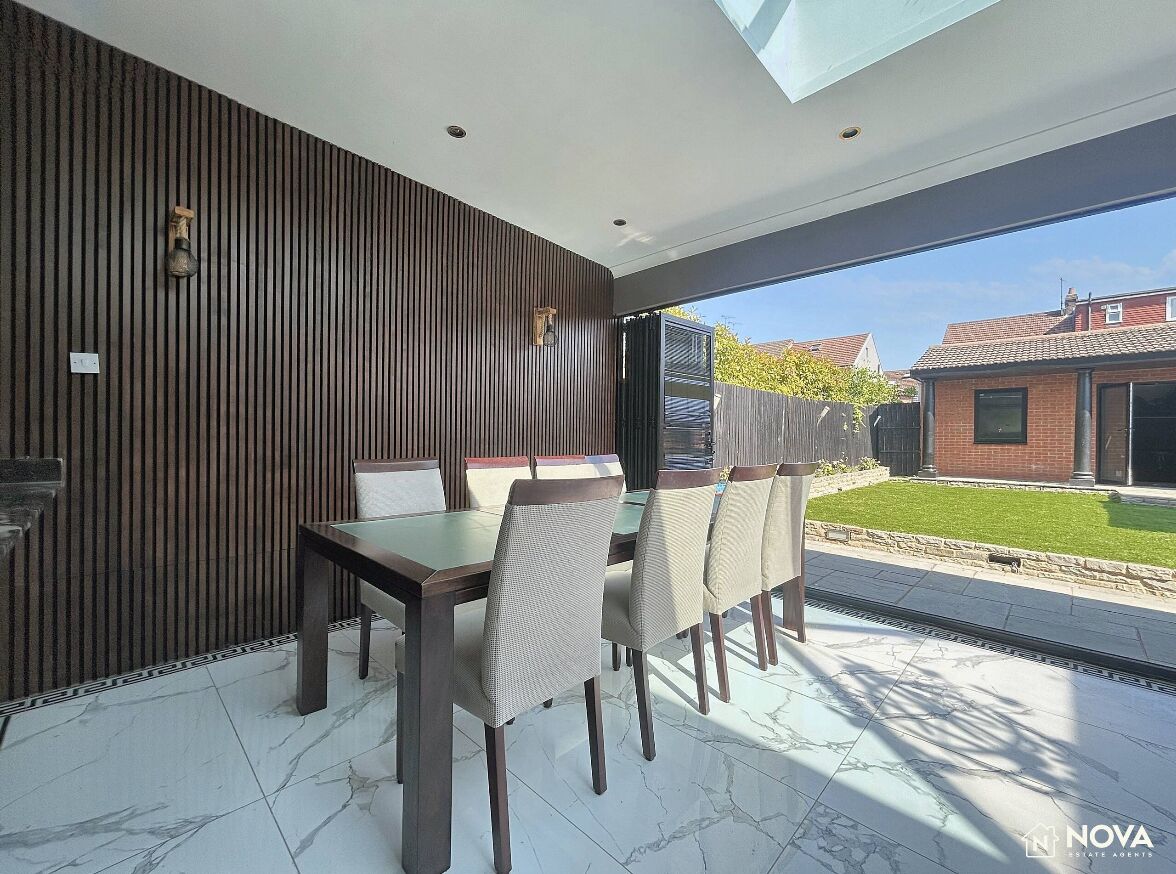 A modern dining area with a glass table and chairs, a wooden wall, and a view of the outside.
