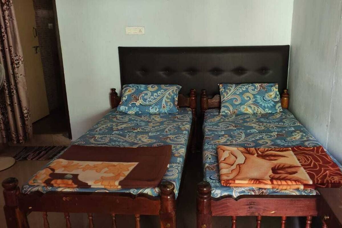 A room with two single beds, each with a patterned bedspread and a brown throw blanket.