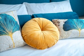 A bed with white bedding, a yellow pillow, and decorative pillows with blue and gold designs.