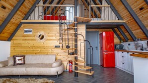 A loft-style room with a wooden ceiling, a sofa, a red refrigerator, and a kitchen area.