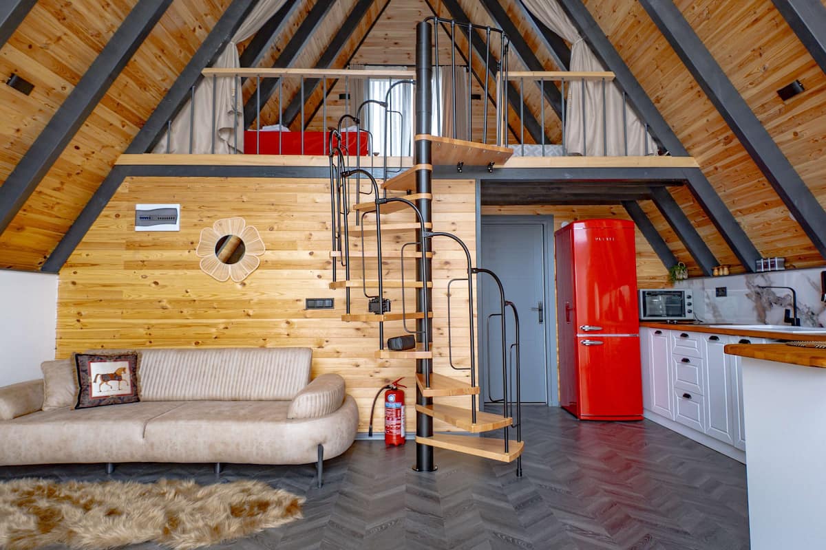 A loft-style room with a wooden ceiling, a sofa, a red refrigerator, and a kitchen area.