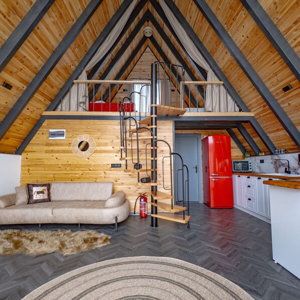 Un espacio tipo loft con techo de madera, un sofá, un refrigerador rojo y una zona de cocina.