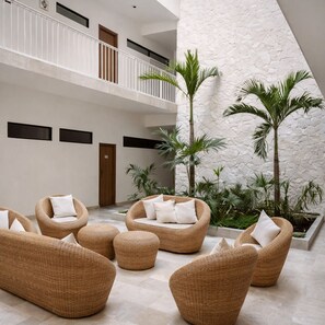 A spacious indoor area with wicker furniture, a white stone wall, and a balcony. - Giada Towers by HEUSHAVEN, Aldea Zama: 2-bed, 2-bath apartment with a private jacuzzi on the main terrace and a large L-shaped terrace with a grill and direct access to the pool. Includes 2 bicycles and access to the gym, movie theater, and ck (Tulum)
