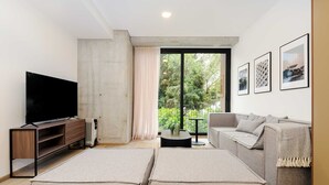 A modern living room with a flat-screen TV, a grey sofa, and a large window with a view of greenery. - w Sophisticated 3BR in the Heart of San Rafael (Mexico City)