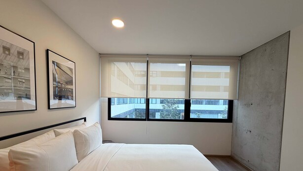 Een slaapkamer met een groot bed, een raam met zonwering en twee ingelijste foto's aan de muur.