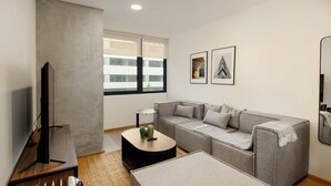 Een moderne woonkamer met een grijze bank, een zwarte salontafel, een televisie en een radiator.