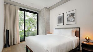 Ett modernt hotellrum med en stor säng, utsikt över grönområden genom en skjutdörr och två inramade tavlor på väggen.