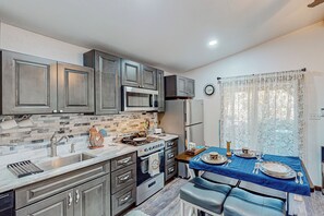 Una cocina moderna con armarios grises, un microondas, una estufa y un lavamanos. Hay una mesa de comedor con platos y cubiertos.