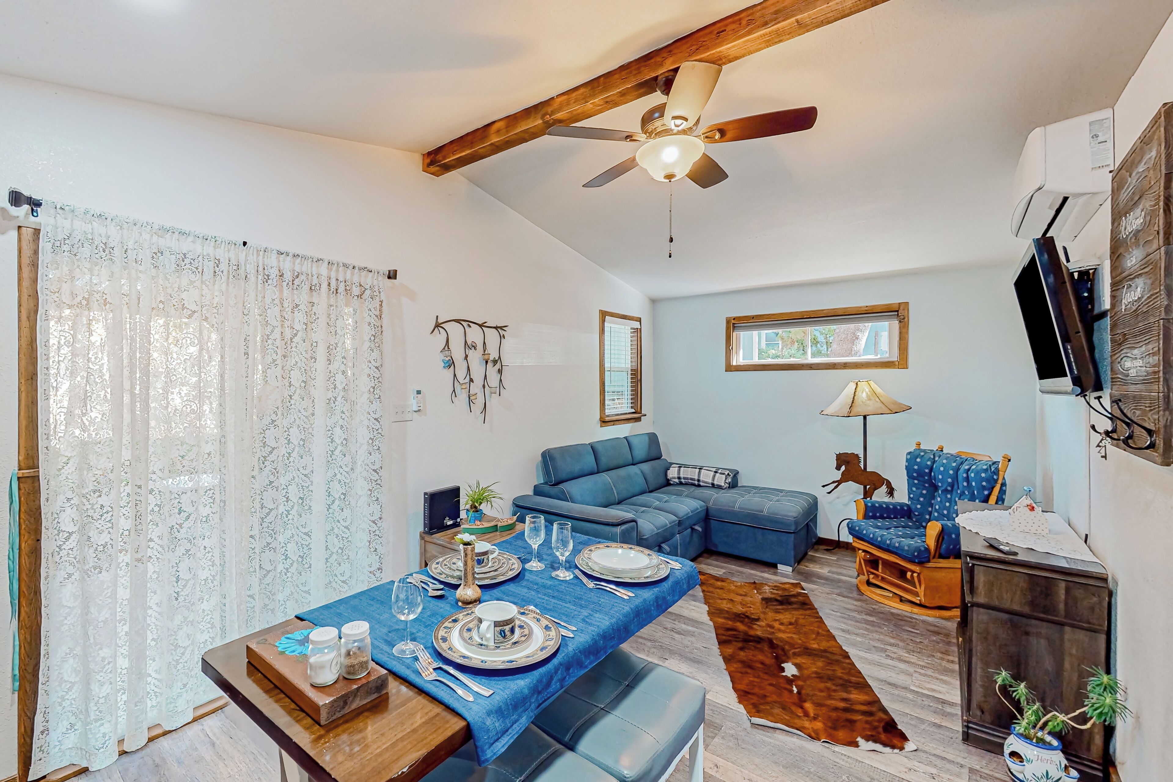 A dining area with a table set for four, a blue sofa, a television, and a ceiling fan.
