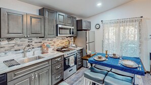 A modern kitchen with grey cabinets, a microwave, a stove, and a sink. There is a dining table set with plates and cutlery. - 1BR Dog-friendly Lakefront Cabin w/ Canoes (Sonora)