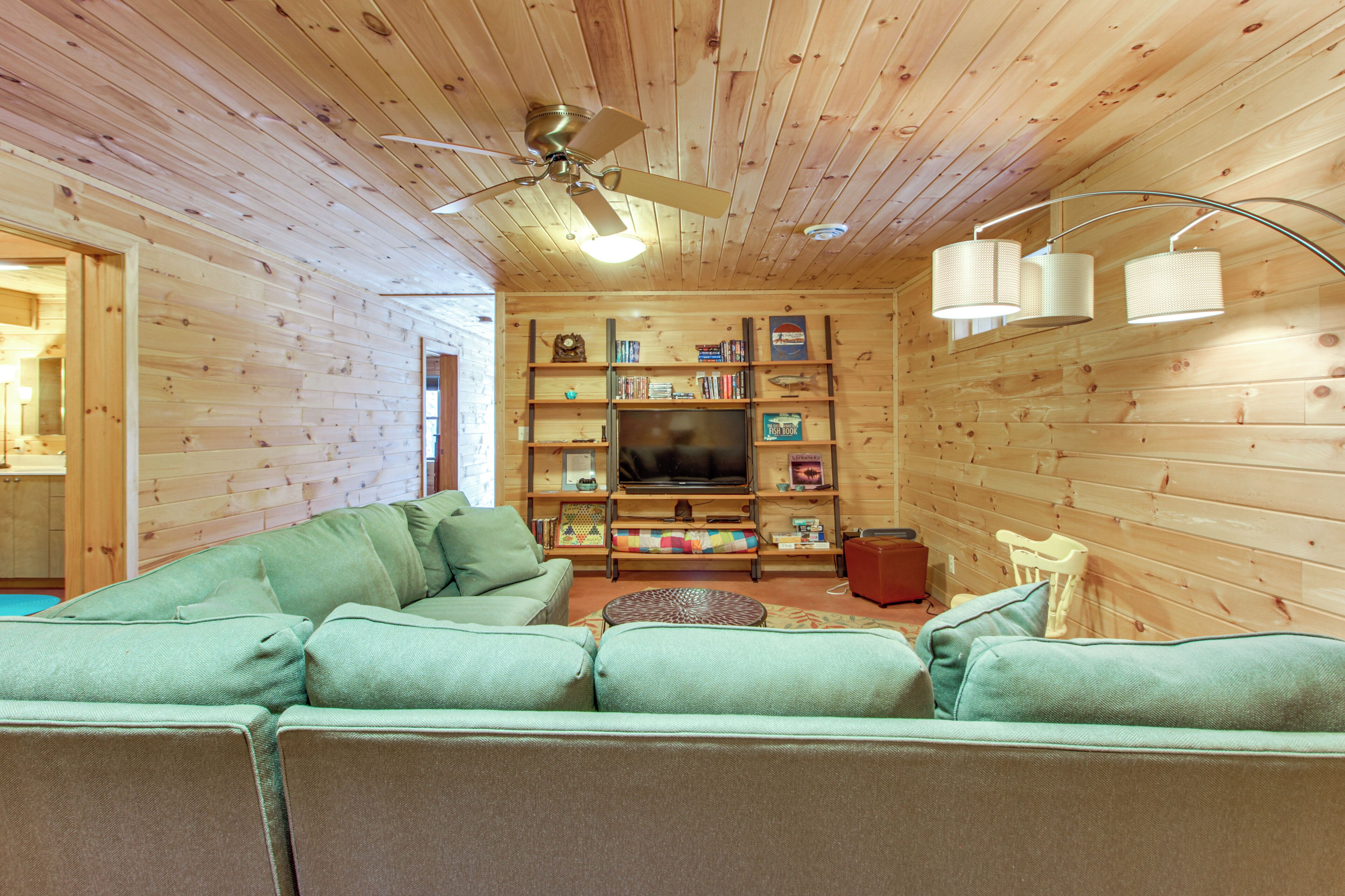 A cozy room with a green sectional sofa, a television, and a bookshelf.