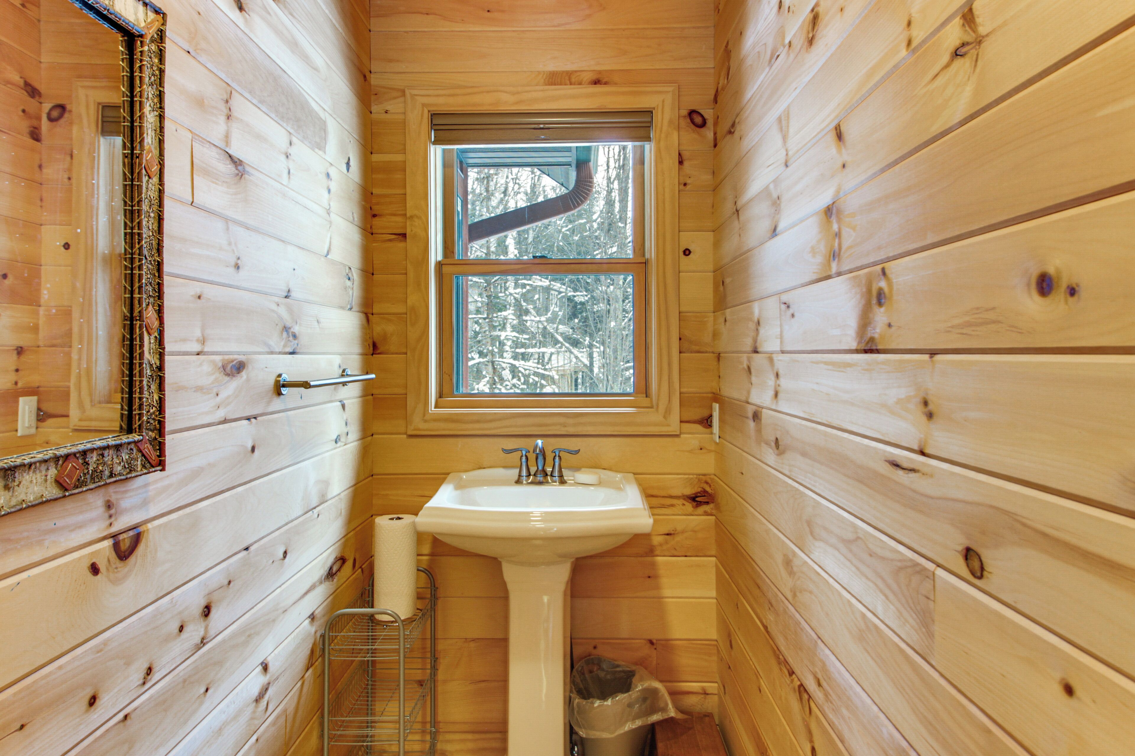 Une salle de bain rustique, avec des murs en bois, une fenêtre, un lavabo et un miroir.