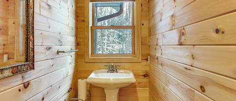Une salle de bain rustique, avec des murs en bois, une fenêtre, un lavabo et un miroir.