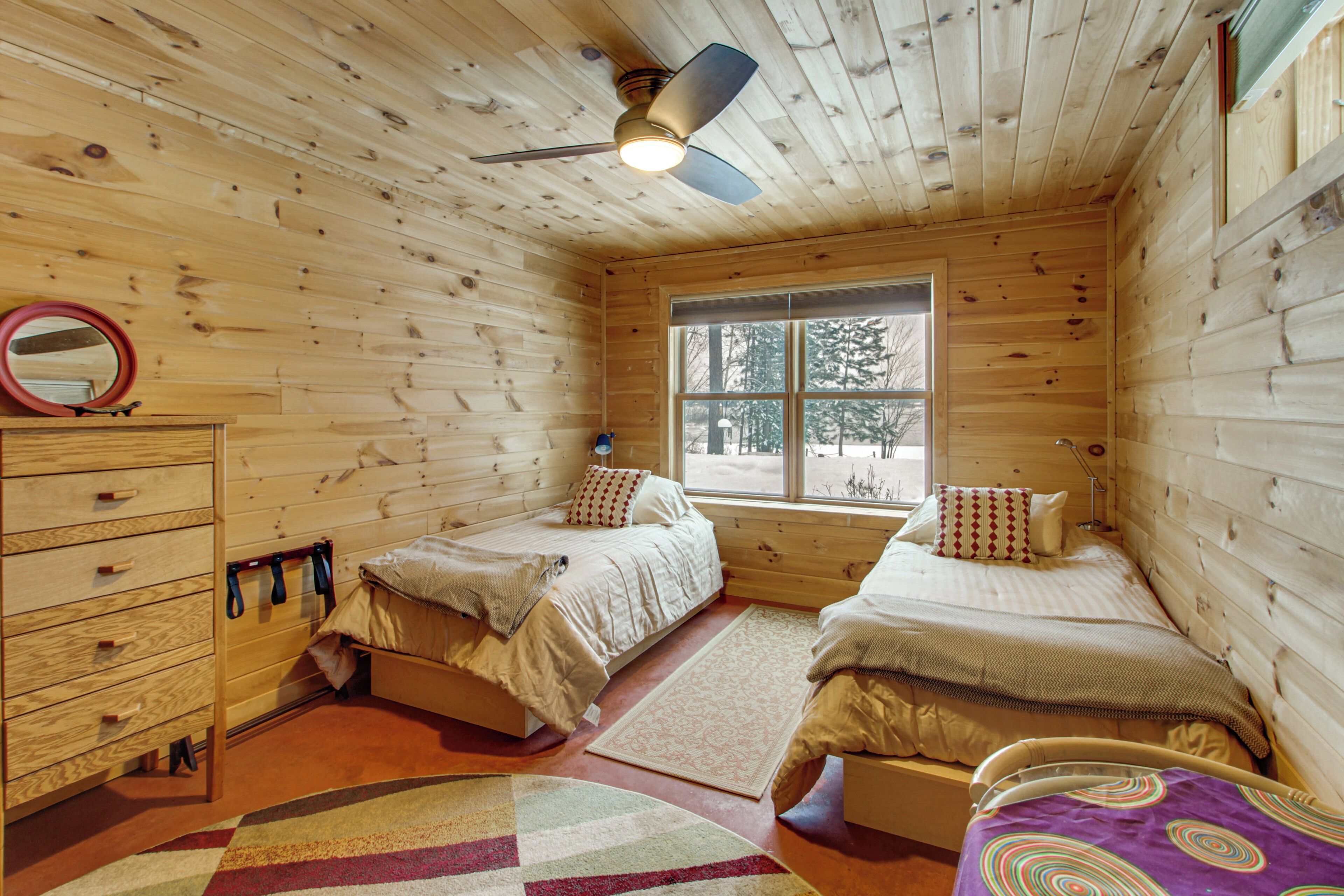 A cabin with two beds, a wooden ceiling, a window, and a mirror.