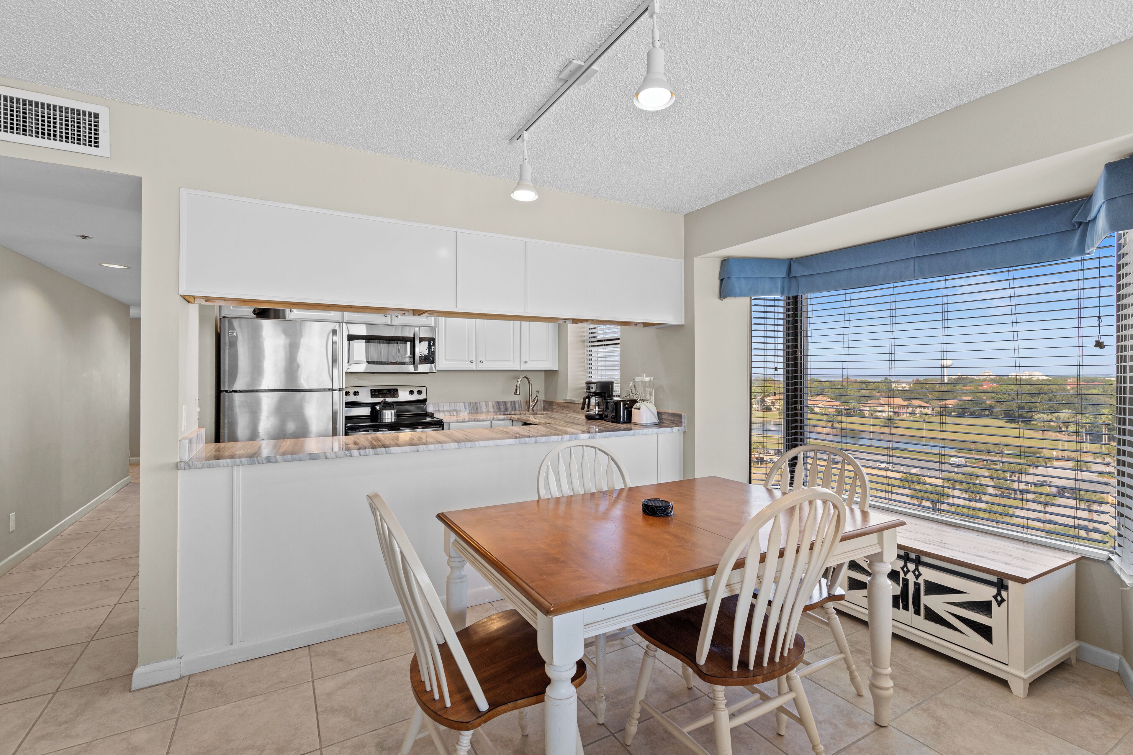 A modern kitchen with white cabinets, stainless steel appliances, and a wooden dining table with chairs.