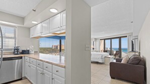 A modern kitchen with white cabinetry and a large window overlooking a cityscape. - New! Beachfront Studio with Covered Balcony, Beach Views, Pool, Tram (Miramar Beach)