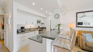A modern kitchen with white cabinetry, a granite countertop, a microwave, and a coffee maker. - Glitter Bay Estate 414 1 Bedroom Apts (Holetown)