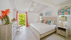 A bedroom with a bed, bedside tables, a dresser, a ceiling fan, and a view of greenery outside. - Glitter Bay Estate 414 1 Bedroom Apts (Holetown)