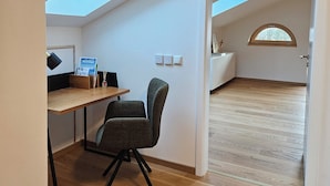Une pièce avec un bureau en bois, une chaise, un puits de lumière et une vue sur un arbre par la fenêtre.