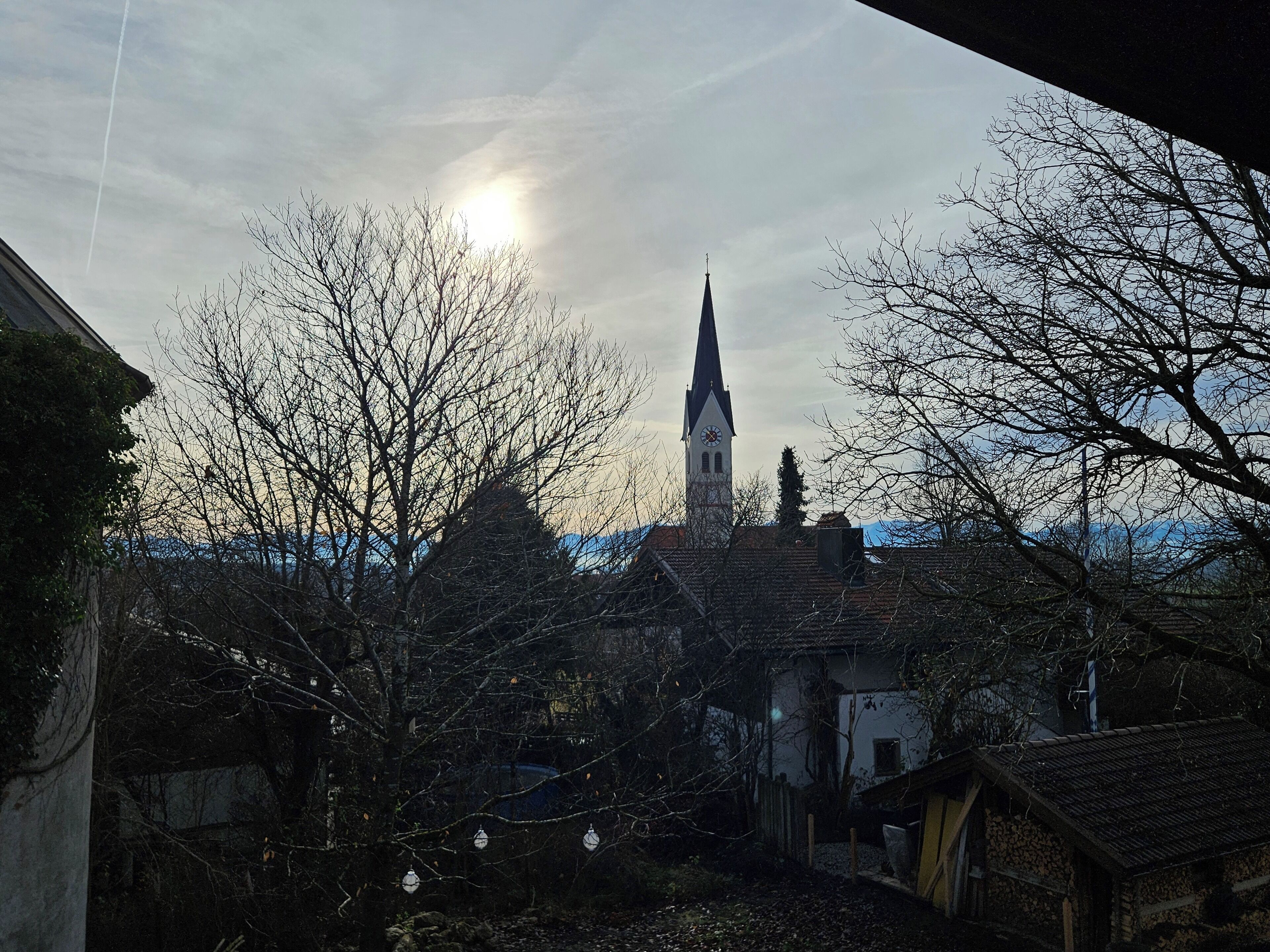 A church with a tall spire, surrounded by leafless trees and houses.