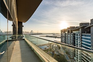 Un balcon moderne avec une balustrade en verre, offrant une vue sur le paysage urbain et une rivière.