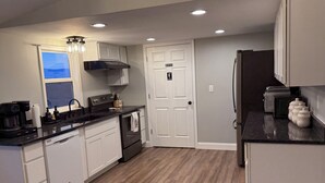 A modern kitchen with white cabinets, a black countertop, and a wooden floor. - Circle F Ranch Bunkhouse- Charming farm stay in Shenandoah county- whole house (Edinburg)