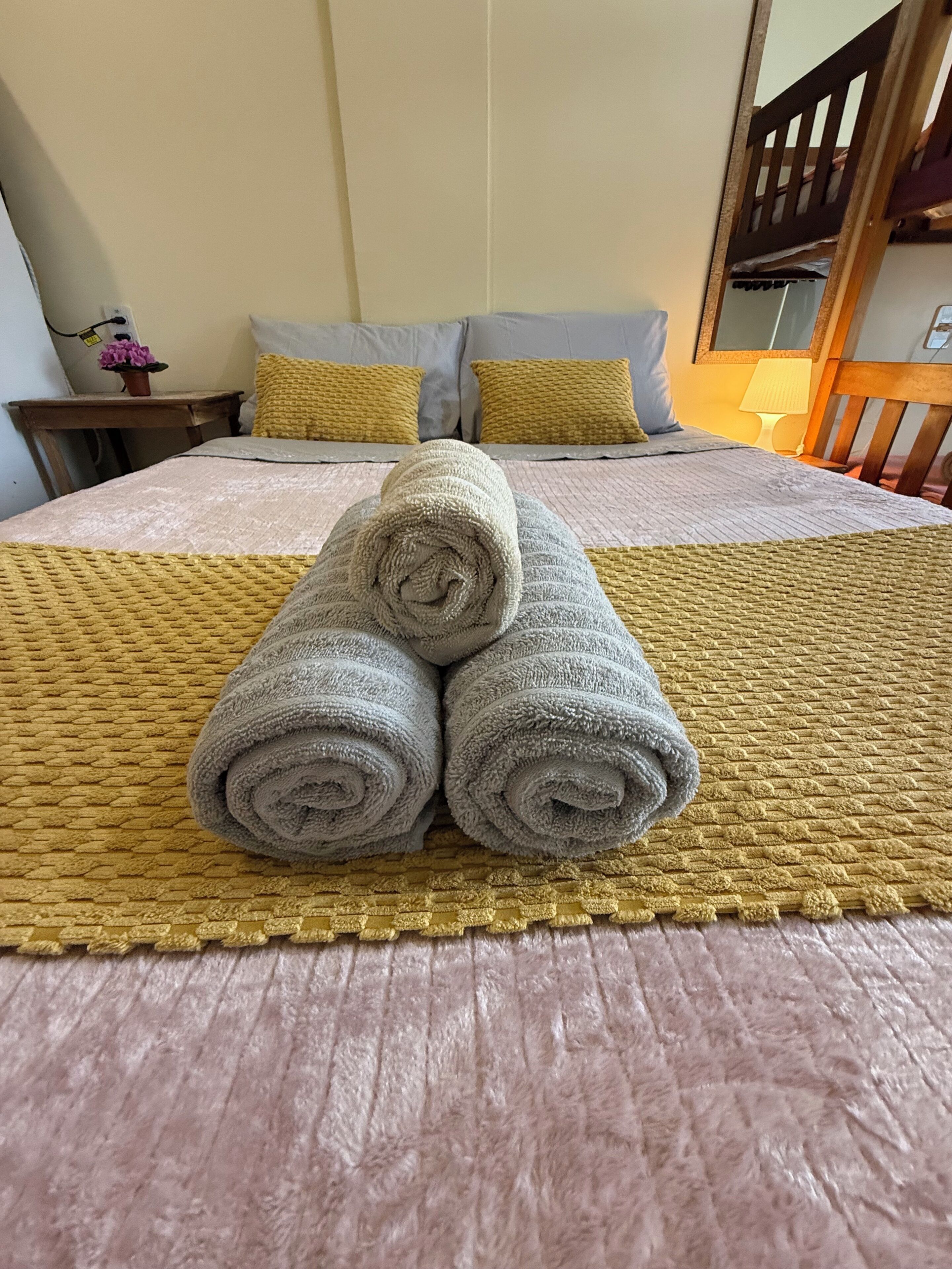 Una cama bien hecha con toallas enrolladas, un cabecero de madera y una mesita de noche con una lámpara.