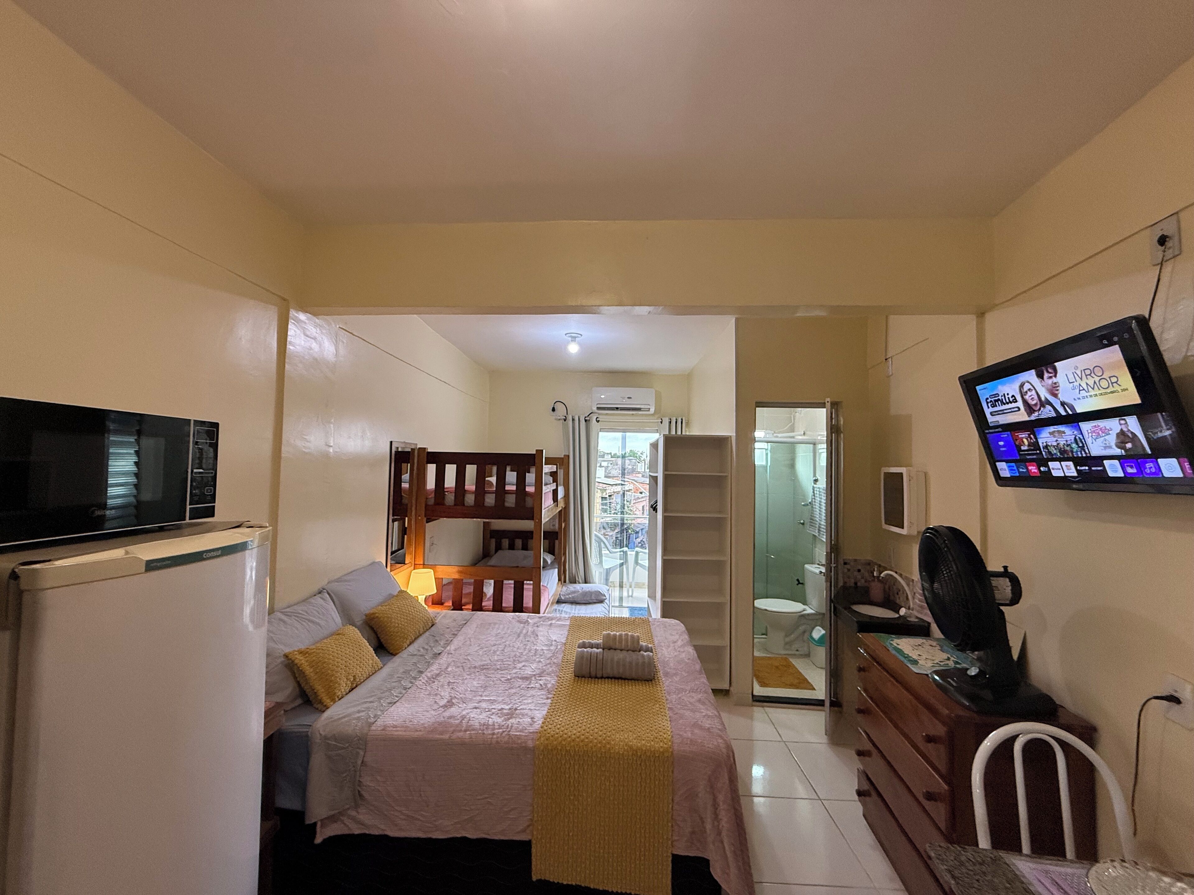 A bedroom with a bed, bedside table, TV, and a small kitchenette.