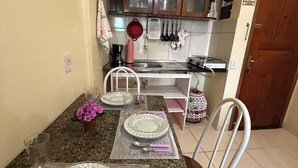 Un coin repas avec une table dressée pour quatre personnes, une cuisine avec des placards en bois et une porte sur laquelle est apposé un panneau « interdiction de fumer ».