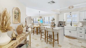 A spacious kitchen with white cabinetry, a dining area with wooden chairs, and a large island. - Beach Villas #606 Gorgeous Beachfront Condo (Fort Myers Beach)