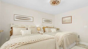 A bedroom with two beds, a chandelier, and artwork on the walls. - Beach Villas #606 Gorgeous Beachfront Condo (Fort Myers Beach)