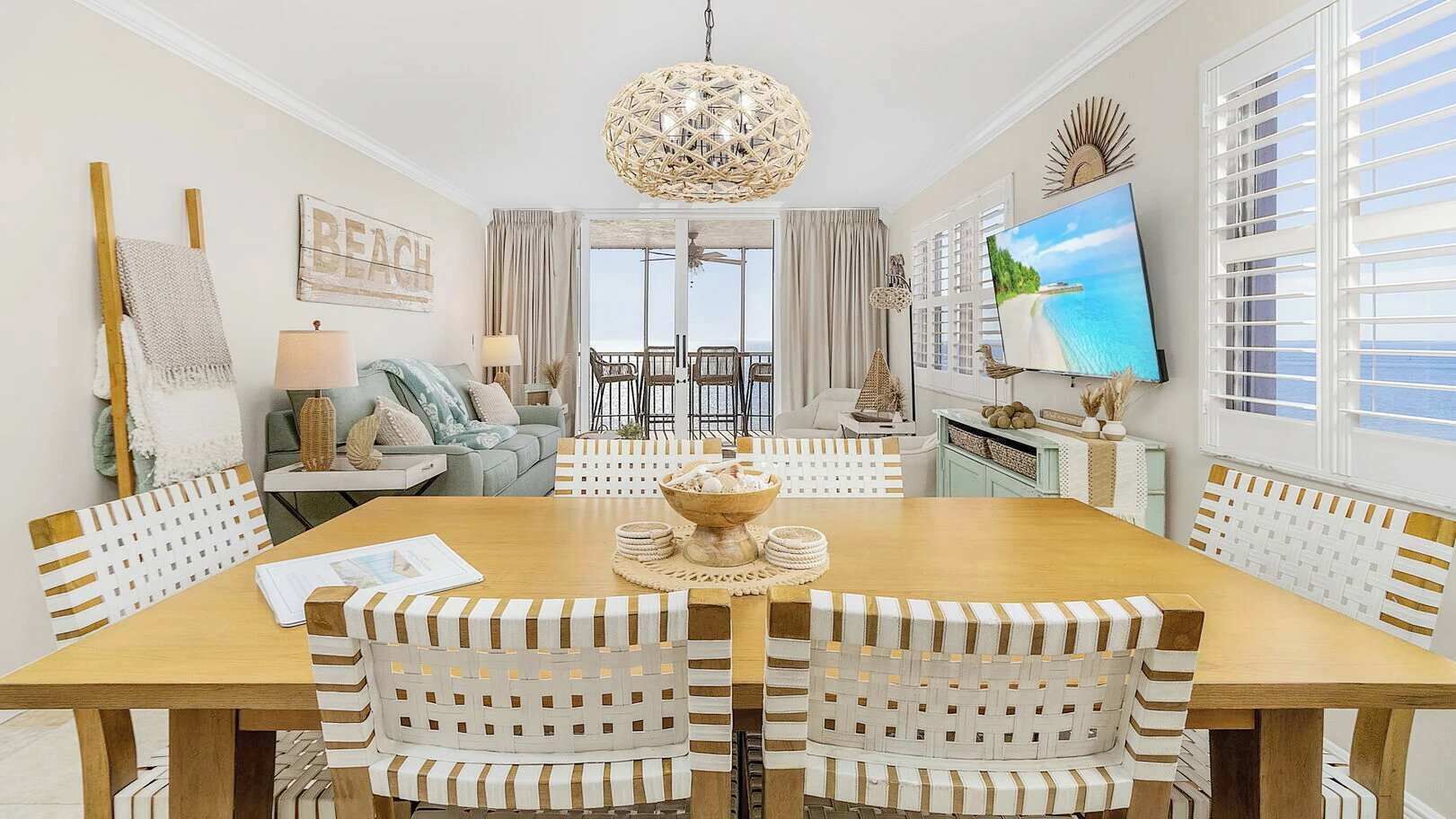 A dining area with a wooden table, white chairs, a central decorative bowl, and a television on the wall.