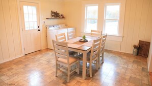 Un coin repas avec une table et des chaises en bois, un poêle et une fenêtre avec des stores.